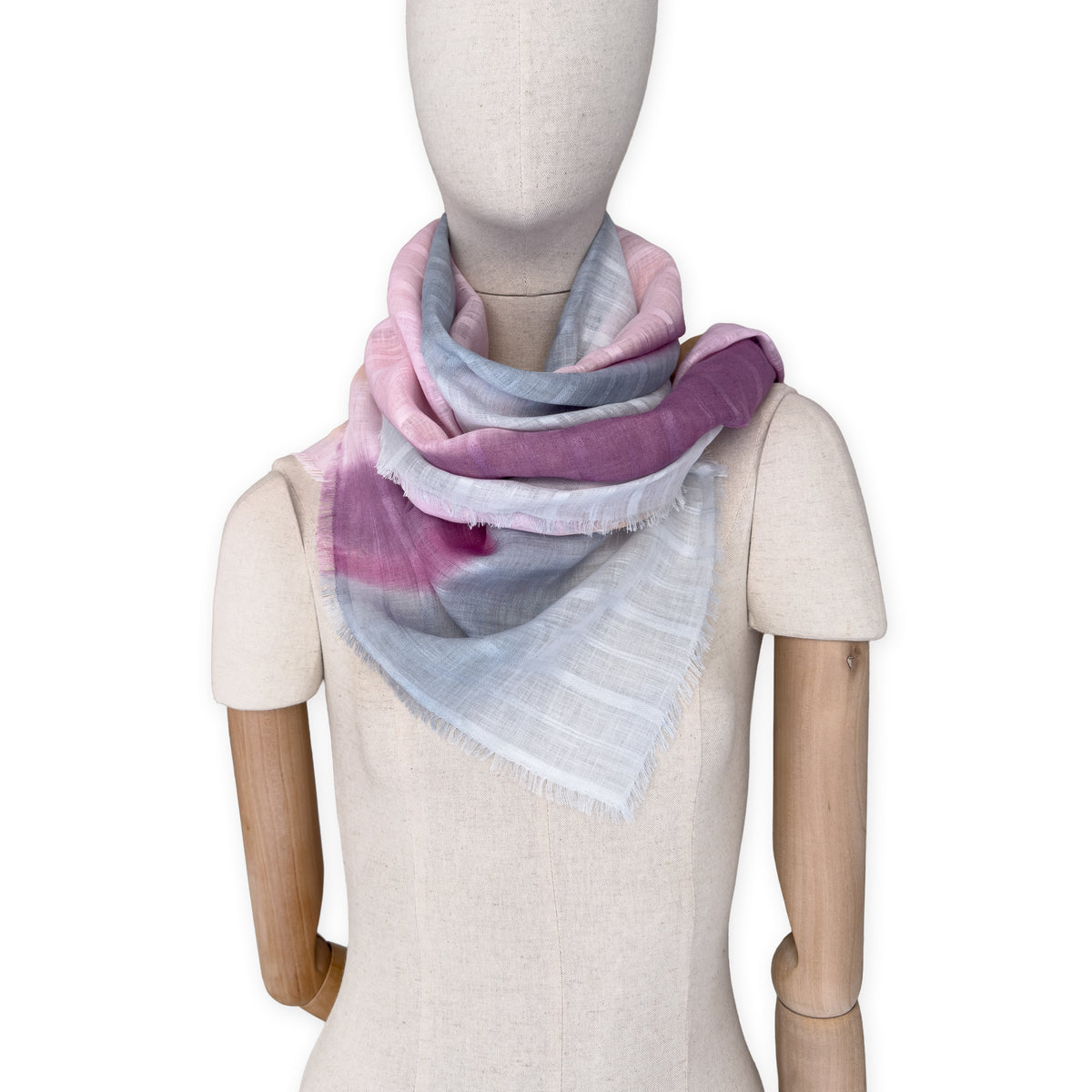 Mannequin wearing a hand-painted Otta pure linen scarf on a white background in 
pink, peach, fuchsia and gray tones. soft, fresh and lightweight, and elegant accessory measuring 70 x 190 cm. Unique artisan scarf with hand-sewn edges, perfect for women and men.
