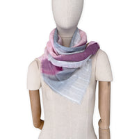 Mannequin wearing a hand-painted Otta pure linen scarf on a white background in 
pink, peach, fuchsia and gray tones. soft, fresh and lightweight, and elegant accessory measuring 70 x 190 cm. Unique artisan scarf with hand-sewn edges, perfect for women and men.
