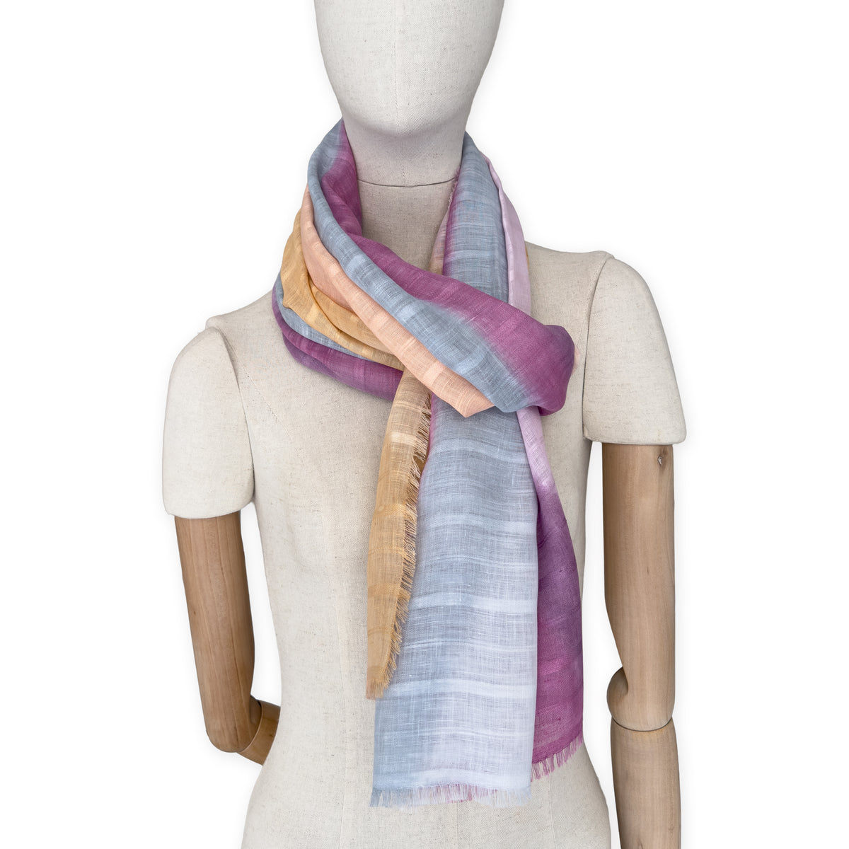 Mannequin wearing a hand-painted Otta pure linen scarf on a white background in 
pink, peach, fuchsia and gray tones. soft, fresh and lightweight, and elegant accessory measuring 70 x 190 cm. Unique artisan scarf with hand-sewn edges, perfect for women and men.
