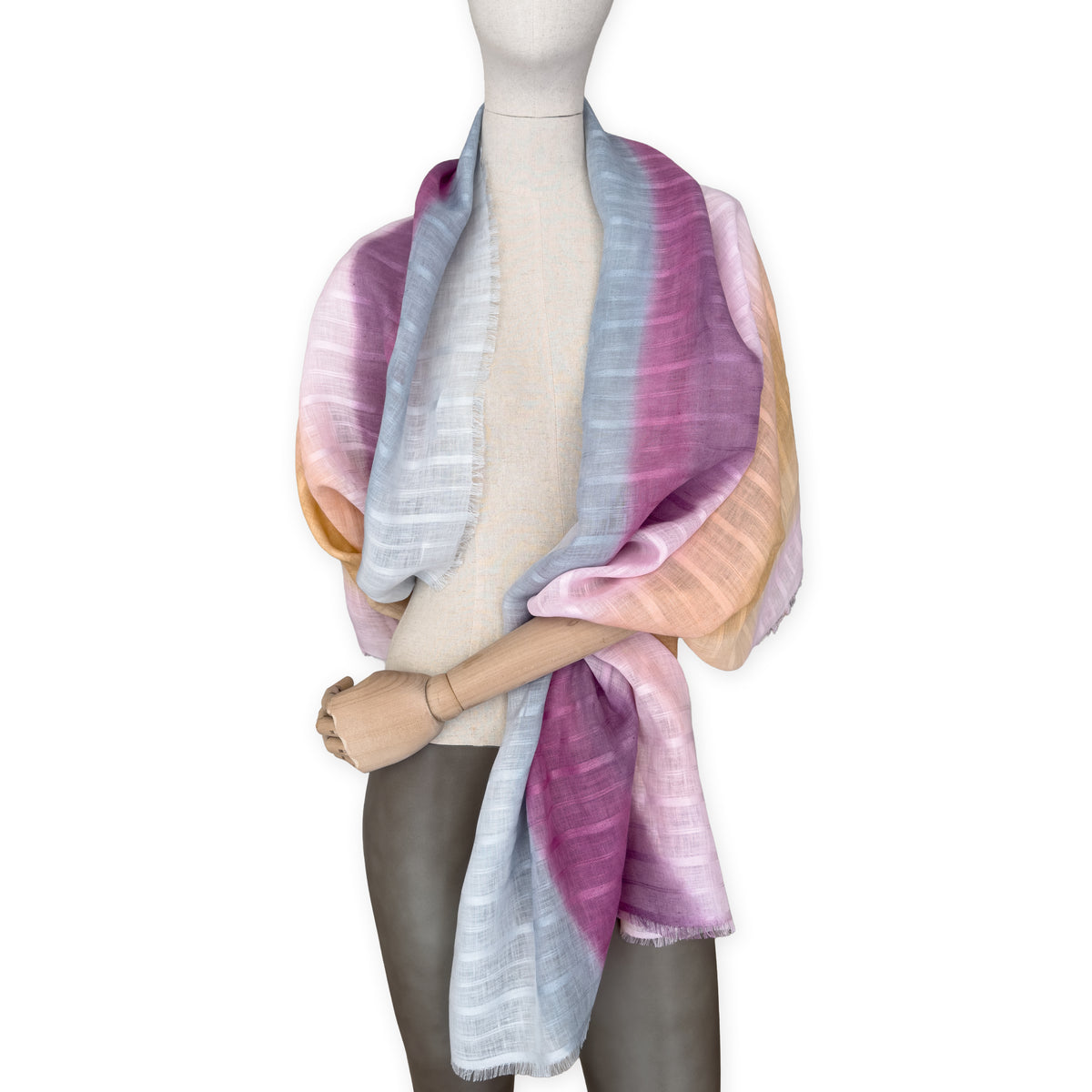 Mannequin wearing a hand-painted Otta pure linen scarf on a white background in 
pink, peach, fuchsia and gray tones. soft, fresh and lightweight, and elegant accessory measuring 70 x 190 cm. Unique artisan scarf with hand-sewn edges, perfect for women and men.
