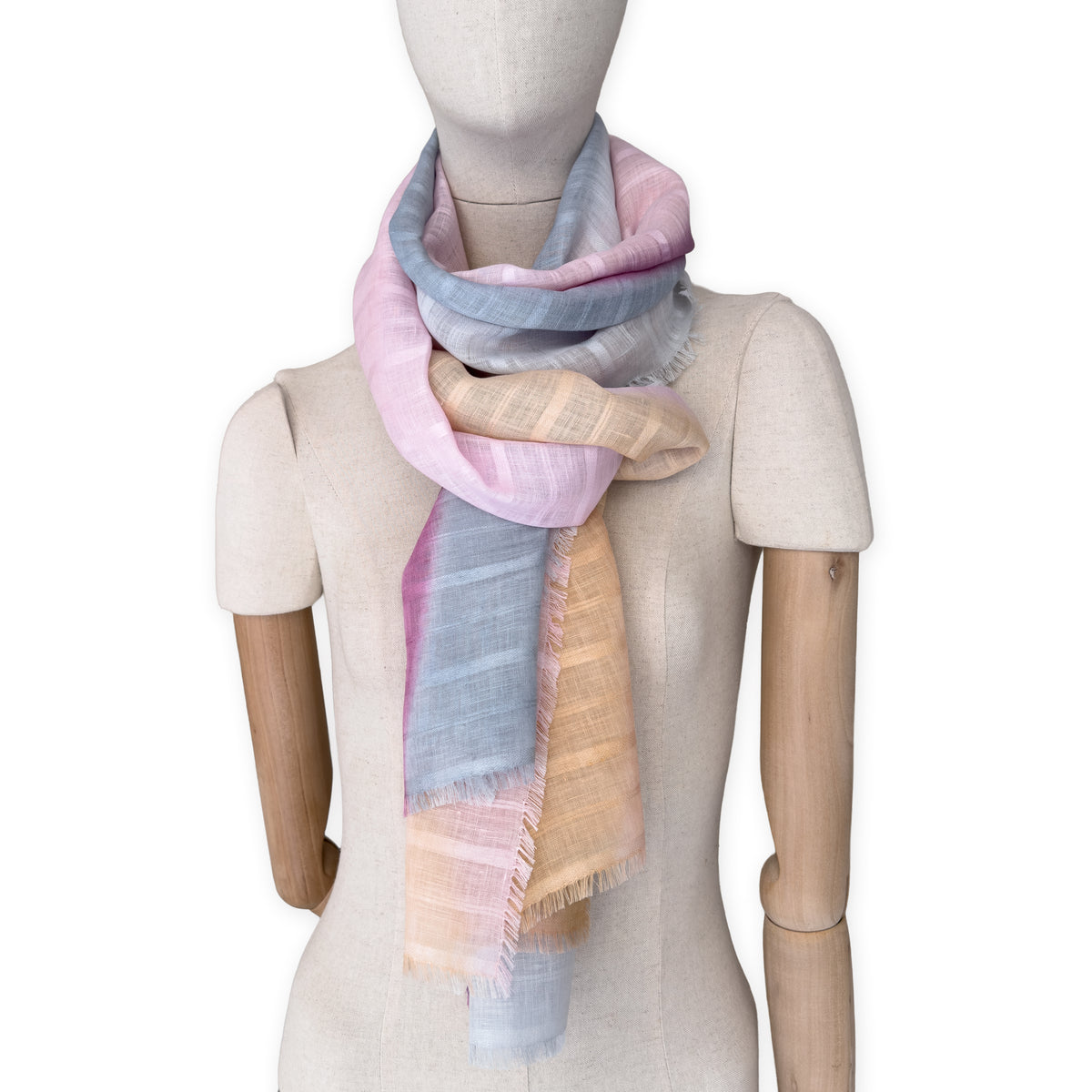 Mannequin wearing a hand-painted Otta pure linen scarf on a white background in 
pink, peach, fuchsia and gray tones. soft, fresh and lightweight, and elegant accessory measuring 70 x 190 cm. Unique artisan scarf with hand-sewn edges, perfect for women and men.
