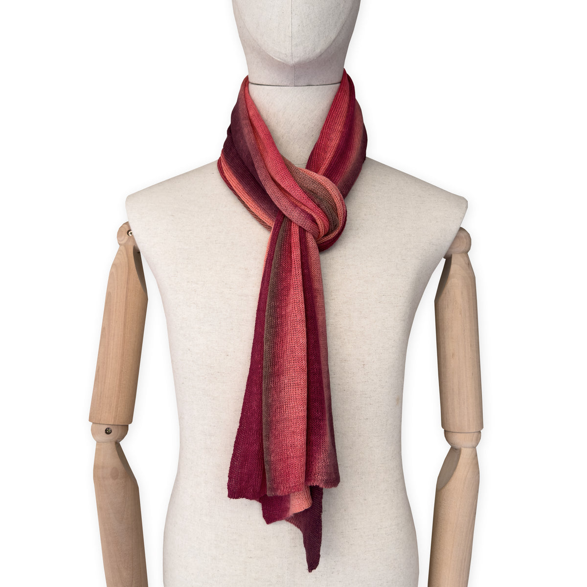 Mannequin wearing a colorful and lightweight linen scarf on a white background. Linen scarf is in shades of red, coral and brown colors. It is hand-painted scarf in measures 32 x 200 cm by otta-italy scarves brand. Luxury Italian linen, soft and lightweight scarf for women and men.
