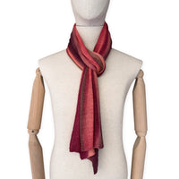 Mannequin wearing a colorful and lightweight linen scarf on a white background. Linen scarf is in shades of red, coral and brown colors. It is hand-painted scarf in measures 32 x 200 cm by otta-italy scarves brand. Luxury Italian linen, soft and lightweight scarf for women and men.
