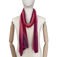 Mannequin wearing a hand-painted Otta pure linen scarf on a white background in 
red and purple tones. soft, fresh and lightweight, and elegant accessory measuring 33 x 205 cm. Unique artisan scarf with hand-sewn edges, perfect for women and men.

