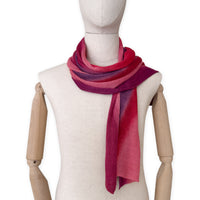 Mannequin wearing a hand-painted Otta pure linen scarf on a white background in 
red and purple tones. soft, fresh and lightweight, and elegant accessory measuring 33 x 205 cm. Unique artisan scarf with hand-sewn edges, perfect for women and men.
