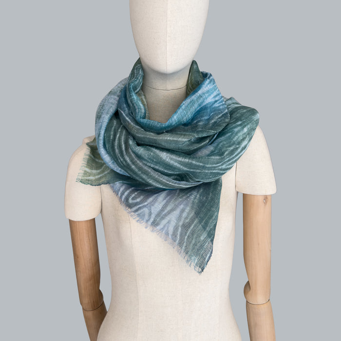 Mannequin wearing scarf on a pastel gray background. Hand-painted linen scarf by Otta-Italy, 52 x 205 cm, featuring 
blue, light blue and green. Luxury Italian pure linen accessory, soft, fresh and lightweight scarf for women and men.
