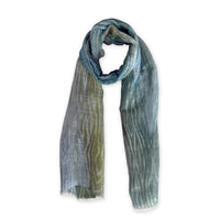 Hand-painted Otta pure linen scarf in 
blue, light blue and green, loosely looped to showcase its full length and delicate texture in white background. Lightweight artisan accessory with hand-sewn edges, measuring 52 x 205 cm.
