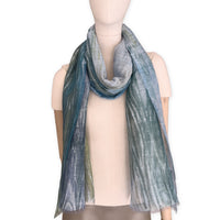 Mannequin wearing a hand-painted Otta pure linen scarf on a white background in 
blue, light blue and green tones. soft, fresh and lightweight, and elegant accessory measuring 52 x 205 cm. Unique artisan scarf with hand-sewn edges, perfect for women and men.
