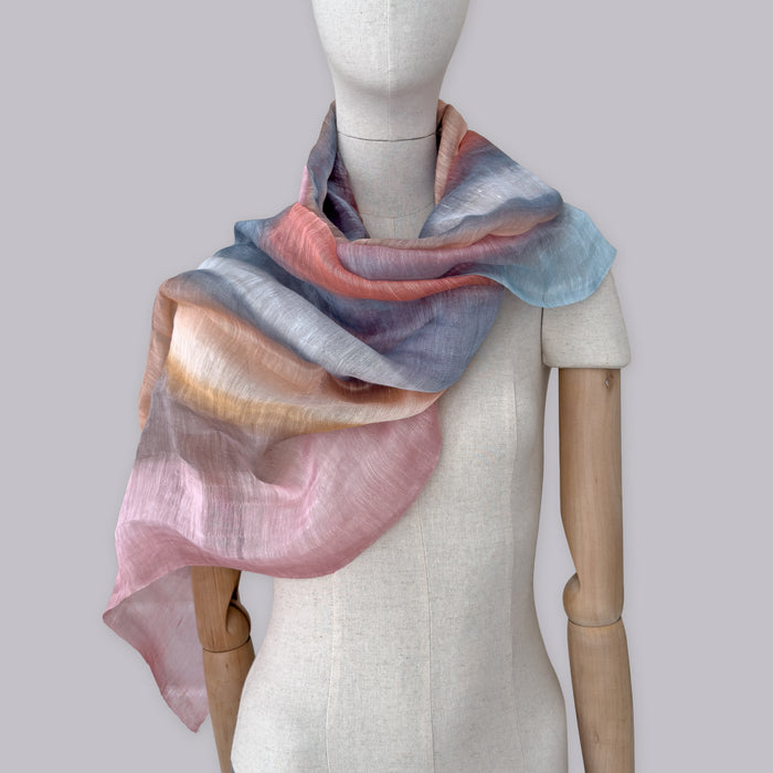 Mannequin wearing scarf on a pastel gray background. Hand-painted linen scarf by Otta-Italy, 52 x 200 cm, featuring 
coral, gray, brown, pink and blue. Luxury Italian pure linen accessory, soft, fresh and lightweight scarf for women and men.
