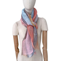 Mannequin wearing a hand-painted Otta pure linen scarf on a white background in 
coral, gray, brown, pink and blue tones. soft, fresh and lightweight, and elegant accessory measuring 52 x 200 cm. Unique artisan scarf with hand-sewn edges, perfect for women and men.
