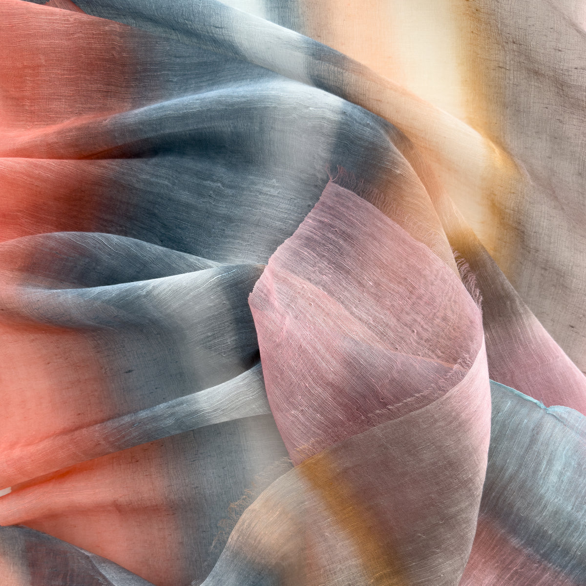 Close-up of soft fabric, a hand-painted Otta pure linen scarf draped softly, showcasing gentle shades of 
coral, gray, brown, pink and blue. Lightweight artisan accessory with delicate hand-sewn edges, measuring 52 x 200 cm.
