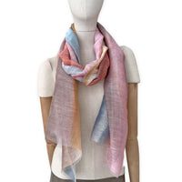 Mannequin wearing a hand-painted Otta pure linen scarf on a white background in 
coral, gray, brown, pink and blue tones. soft, fresh and lightweight, and elegant accessory measuring 52 x 200 cm. Unique artisan scarf with hand-sewn edges, perfect for women and men.
