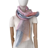 Mannequin wearing a hand-painted Otta pure linen scarf on a white background in 
coral, gray, brown, pink and blue tones. soft, fresh and lightweight, and elegant accessory measuring 52 x 200 cm. Unique artisan scarf with hand-sewn edges, perfect for women and men.
