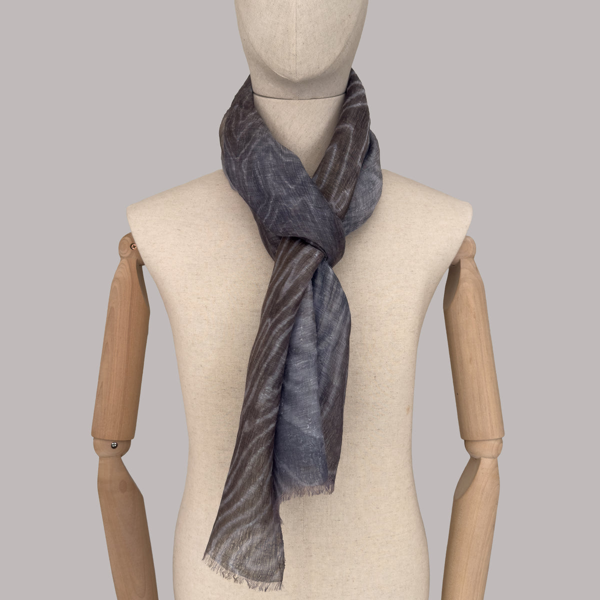 
Mannequin wearing a hand-painted Otta pure linen scarf on a gray background in 
brown, gray and blue tones. soft, fresh and lightweight, and elegant accessory measuring 51x 202 cm. Unique artisan scarf with hand-sewn edges, perfect for women and men.
