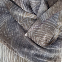 Close-up of soft fabric, a hand-painted Otta pure linen scarf draped softly, showcasing gentle shades of 
brown, gray and blue. Lightweight artisan accessory with delicate hand-sewn edges, measuring 51x 202 cm.
