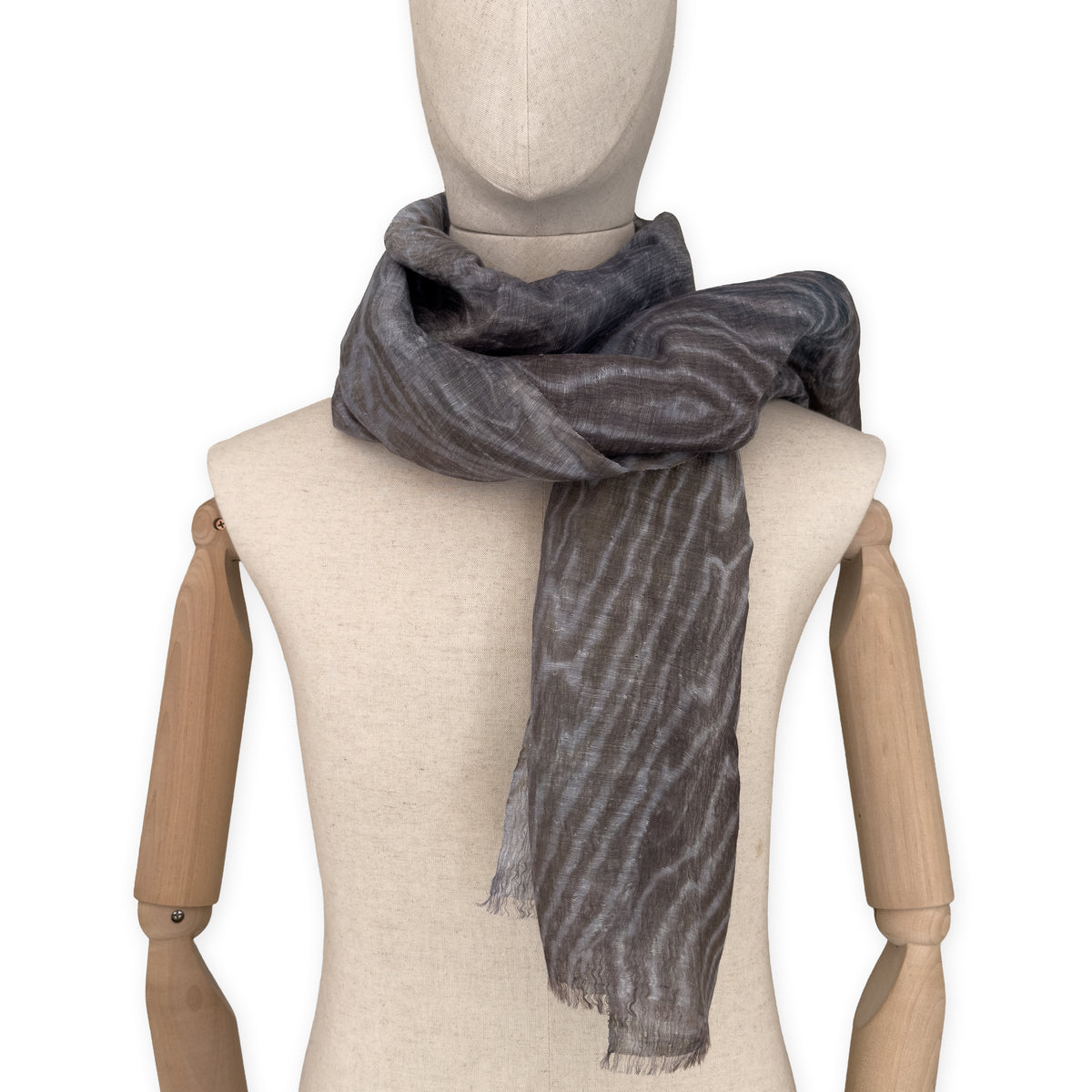 
Mannequin wearing a hand-painted Otta pure linen scarf on a white background in 
brown, gray and blue tones. soft, fresh and lightweight, and elegant accessory measuring 51x 202 cm. Unique artisan scarf with hand-sewn edges, perfect for women and men.
