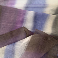 Close-up of a hand-painted Otta linen silk blend scarf showcasing soft shades of indigo, light blue, purple, brown and beige with delicate hand-fringed edges.
