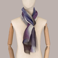 Mannequin wearing a hand-painted linen silk blend scarf by Otta-Italy, gray background. Indigo, light blue, purple, brown and beige. 52x201 cm.
