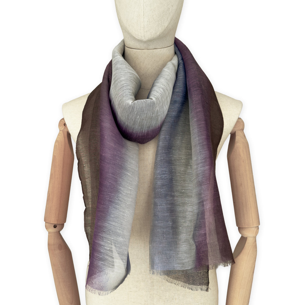 Mannequin wearing an elegant hand-painted Otta linen silk blend scarf on a white background. Indigo, light blue, purple, brown and beige tones.

