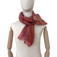 Mannequin wearing a hand-painted Otta pure linen scarf on a white background in 
brown and red tones. soft, fresh and lightweight, and elegant accessory measuring 203 x 50 cm. Unique artisan scarf with hand-sewn edges, perfect for women and men.

