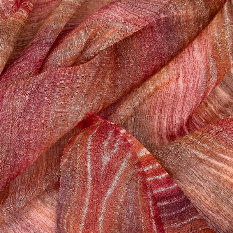 Close-up of soft fabric, a hand-painted Otta pure linen scarf draped softly, showcasing gentle shades of 
brown and red. Lightweight artisan accessory with delicate hand-sewn edges, measuring 203 x 50 cm.
