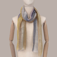 Mannequin wearing a hand-painted linen silk blend scarf by Otta-Italy, beige background. Yellow, ochre, sapphire, and gray wearable art. 52x200 cm.
