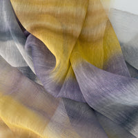 Close-up of a hand-painted Otta-Italy linen silk blend scarf showcasing rich shades of yellow, ochre, sapphire, and gray with delicate hand-fringed edges.
