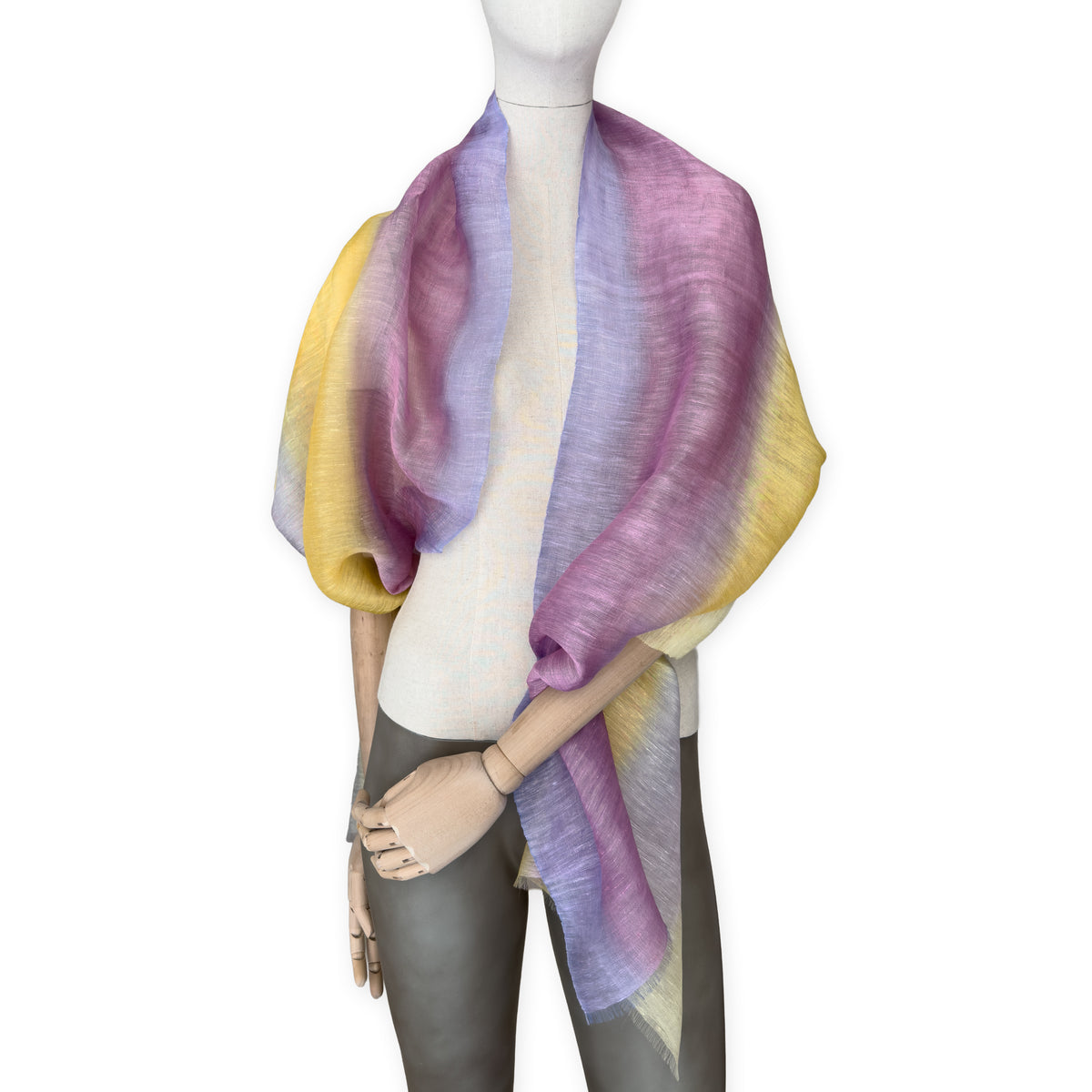 Mannequin wearing a hand-painted Otta pure linen scarf on a white background in 
yellow, purple and lilac tones. soft, fresh and lightweight, and elegant accessory measuring 52 x 200 cm. Unique artisan scarf with hand-sewn edges, perfect for women and men.
