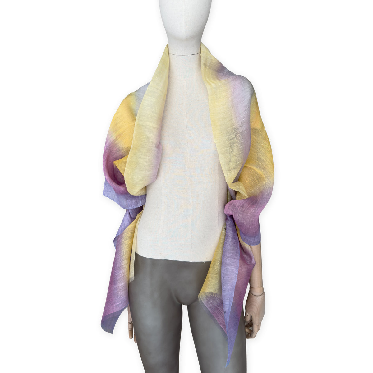 Mannequin wearing a hand-painted Otta pure linen scarf on a white background in 
yellow, purple and lilac tones. soft, fresh and lightweight, and elegant accessory measuring 52 x 200 cm. Unique artisan scarf with hand-sewn edges, perfect for women and men.
