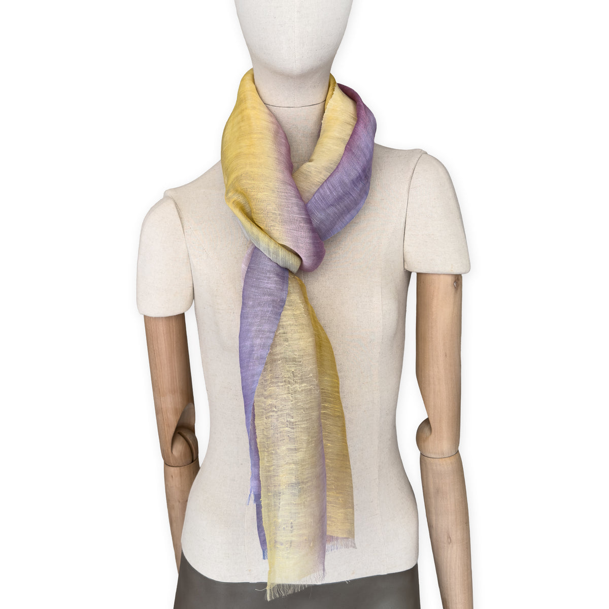 Mannequin wearing a hand-painted Otta pure linen scarf on a white background in 
yellow, purple and lilac tones. soft, fresh and lightweight, and elegant accessory measuring 52 x 200 cm. Unique artisan scarf with hand-sewn edges, perfect for women and men.
