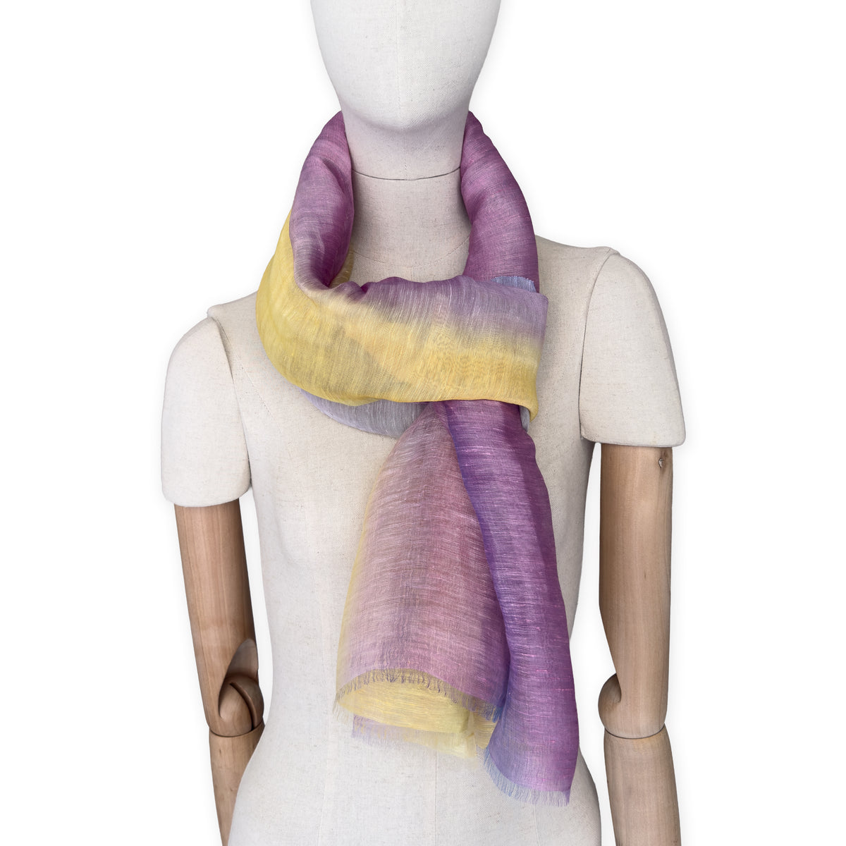 Mannequin wearing a hand-painted Otta pure linen scarf on a white background in 
yellow, purple and lilac tones. soft, fresh and lightweight, and elegant accessory measuring 52 x 200 cm. Unique artisan scarf with hand-sewn edges, perfect for women and men.
