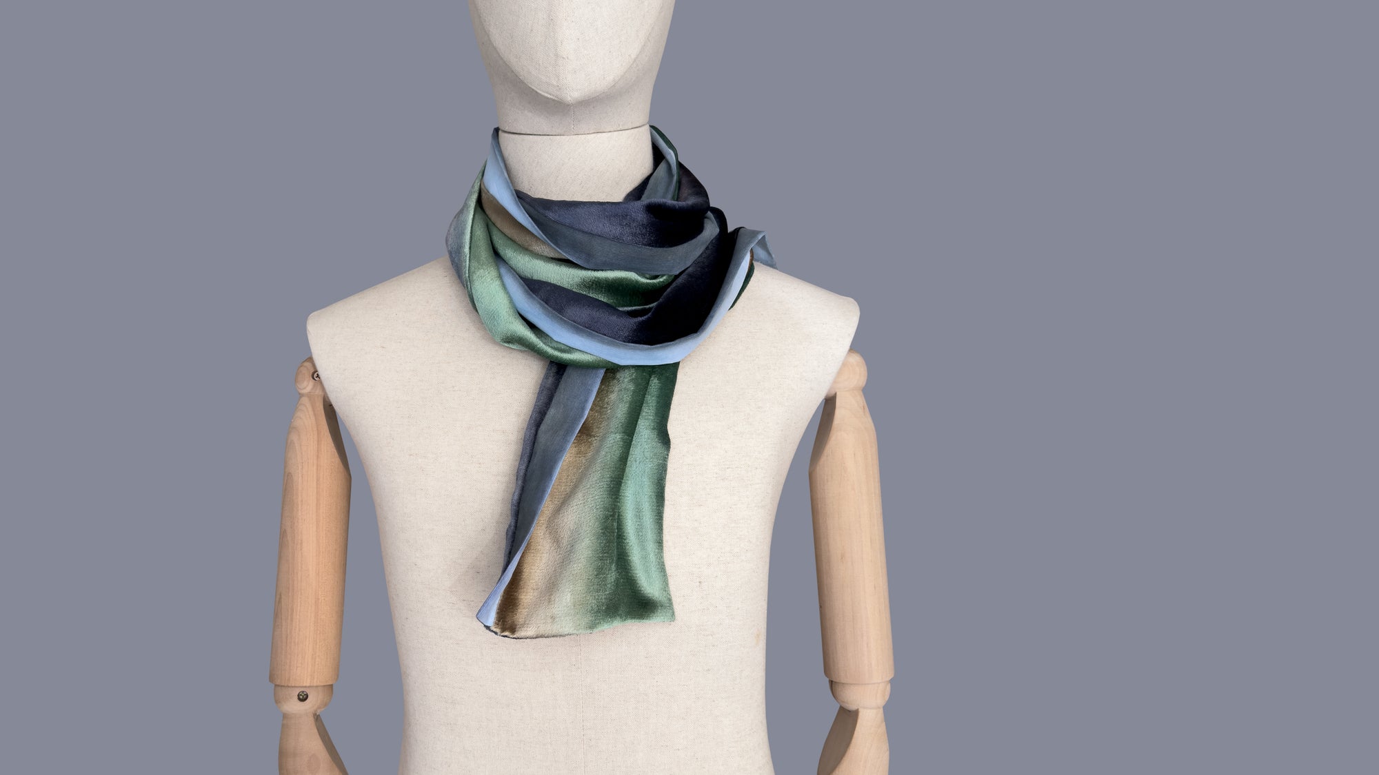 Mannequin wearing a colorful velvet scarf on a white background. Velvet scarf is in shades of green, beige and blue navy colors. It is hand-painted scarf in measures 182 x 18 cm by otta-italy scarves brand.
