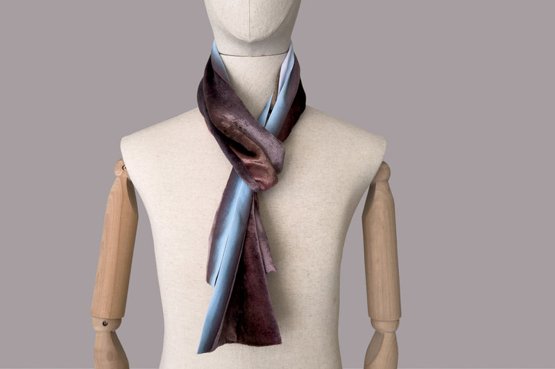 Mannequin wearing a colorful velvet scarf on a white background. Velvet scarf is in shades of brown and blue colors. It is hand-painted scarf in measures 180 x 18 cm by otta-italy scarves brand.
