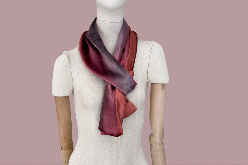 Mannequin wearing a colorful velvet scarf on a white background. Velvet scarf is in shades of red and purple colors. It is hand-painted scarf in measures 184 x 17 cm by otta-italy scarves brand