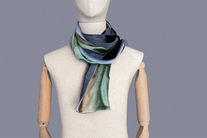 Mannequin wearing a colorful velvet scarf on a white background. Velvet scarf is in shades of green, beige and blue navy colors. It is hand-painted scarf in measures 182 x 18 cm by otta-italy scarves brand.

