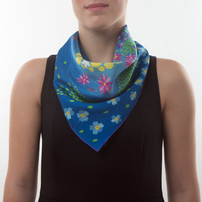 Mannequin wearing an elegant exclusive design Otta silk twill scarf on a white background. Primavera Persiana Blue tones with delicate hand-rolled edges.