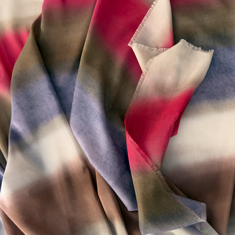 Close-up of a hand-painted Otta silk cotton blend scarf draped softly, showcasing gentle shades of 
brown, beige, red and purple. Lightweight artisan accessory with delicate hand-fringed edges, measuring 70 x 190 cm.
