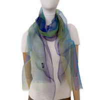 Mannequin wearing an elegant hand-painted Otta pure silk organza scarf on a gray background. Blue, green and violet tones.
