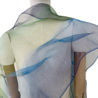 Mannequin wearing an elegant hand-painted Otta pure silk organza scarf on a gray background. Blue, green and violet tones. Close up.