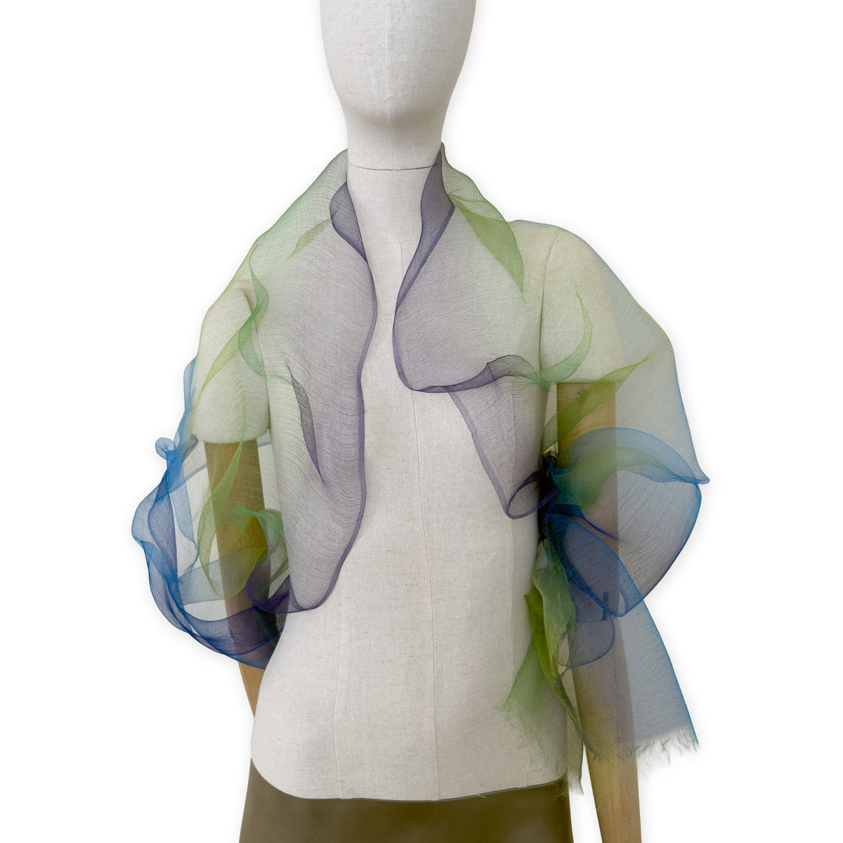 Mannequin wearing an elegant hand-painted Otta pure silk organza scarf on a gray background. Blue, green and violet tones.
