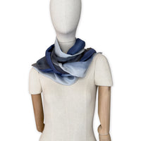 Mannequin wearing a colorful and lightweight silk scarf on a white background. Silk scarf is in shades of gray and midnight blue colors. It is hand-painted scarf in measures 24 x 168 cm by otta-italy scarves brand.
