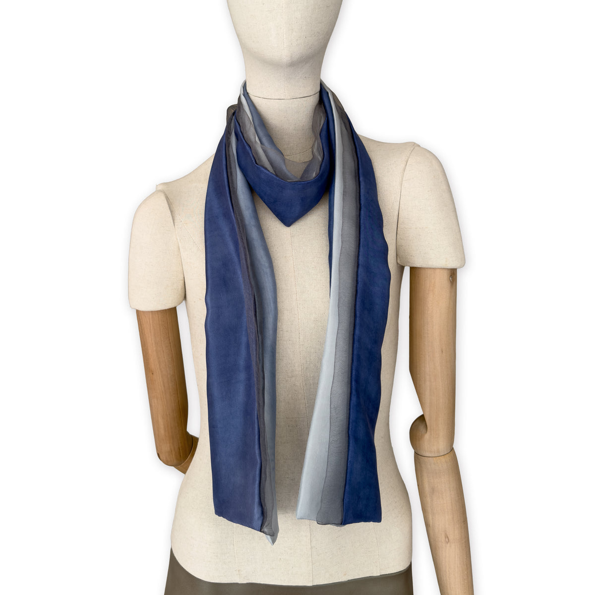 Mannequin wearing a colorful and lightweight silk scarf on a white background. Silk scarf is in shades of gray and midnight blue colors. It is hand-painted scarf in measures 24 x 168 cm by otta-italy scarves brand.

