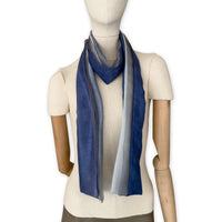 Mannequin wearing a colorful and lightweight silk scarf on a white background. Silk scarf is in shades of gray and midnight blue colors. It is hand-painted scarf in measures 24 x 168 cm by otta-italy scarves brand.
