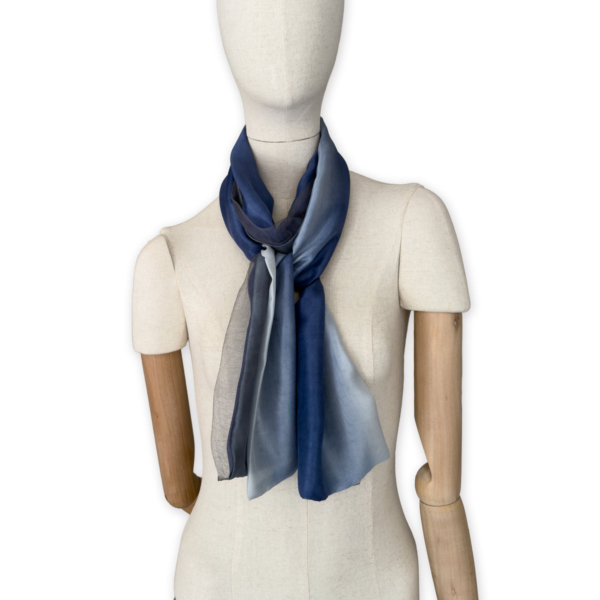 Mannequin wearing a colorful and lightweight silk scarf on a white background. Silk scarf is in shades of gray and midnight blue colors. It is hand-painted scarf in measures 24 x 168 cm by otta-italy scarves brand.
