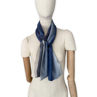 Mannequin wearing a colorful and lightweight silk scarf on a white background. Silk scarf is in shades of gray and midnight blue colors. It is hand-painted scarf in measures 24 x 168 cm by otta-italy scarves brand.
