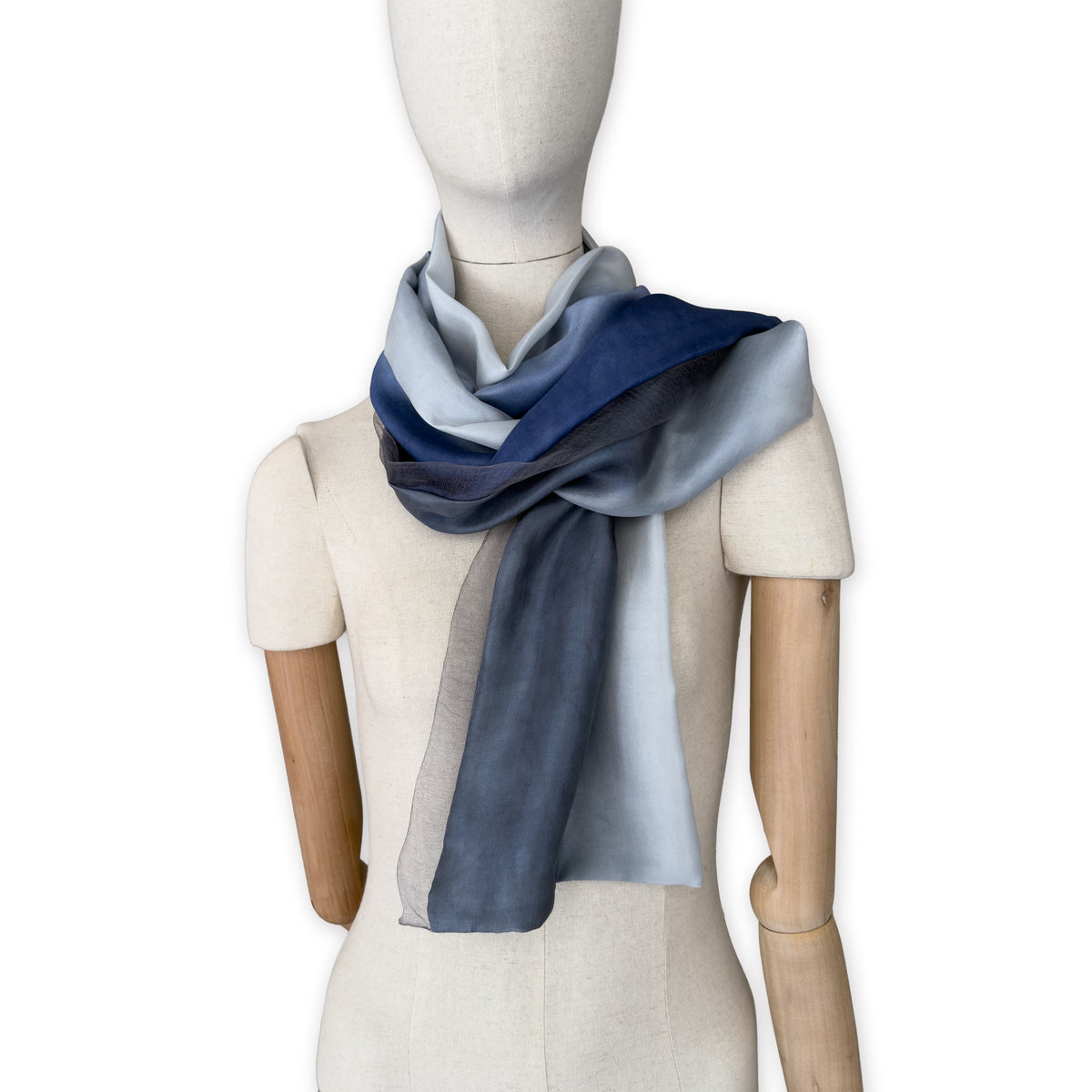 Mannequin wearing a colorful and lightweight silk scarf on a white background. Silk scarf is in shades of gray and midnight blue colors. It is hand-painted scarf in measures 24 x 168 cm by otta-italy scarves brand.
