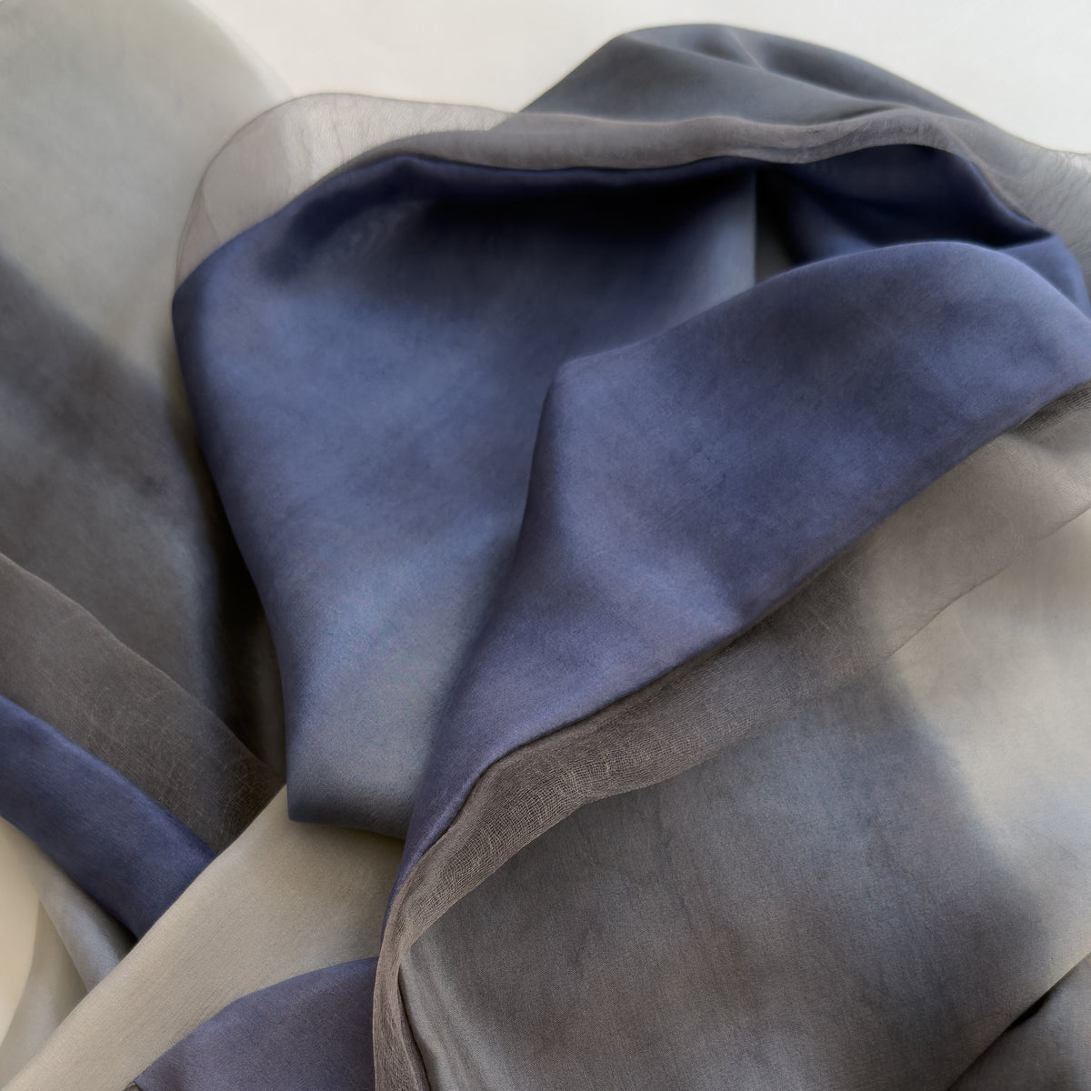 Close-up of fabric. Hand-painted silk scarf by Otta-Italy, 24 x 168 cm, featuring gray and midnight blue colors. Luxury Italian silk scarf, soft and lightweight scarf for women and men.
