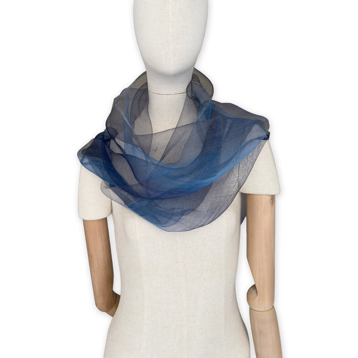 Mannequin wearing a colorful and lightweight silk scarf on a white background. Silk scarf is in shades of gray, midnight blue and blue colors. It is hand-painted scarf in measures 50 x 200 cm by otta-italy scarves brand.
