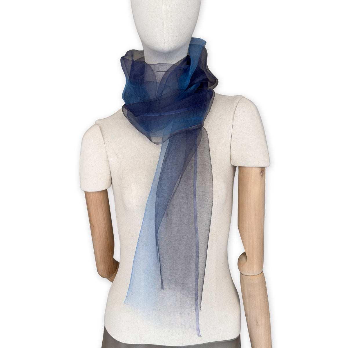 Mannequin wearing a colorful and lightweight silk scarf on a white background. Silk scarf is in shades of gray, midnight blue and blue colors. It is hand-painted scarf in measures 50 x 200 cm by otta-italy scarves brand.
