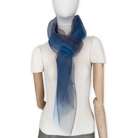 Mannequin wearing a colorful and lightweight silk scarf on a white background. Silk scarf is in shades of gray, midnight blue and blue colors. It is hand-painted scarf in measures 50 x 200 cm by otta-italy scarves brand.
